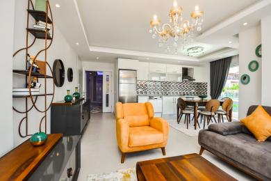 Das helle Wohnzimmer der Alanya-Wohnung verfügt über eine moderne Küche, stilvolle Möbel und einen eleganten Kronleuchter, wodurch eine einladende Atmosphäre geschaffen wird.