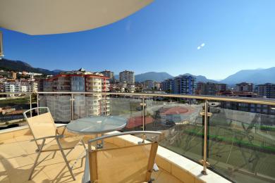Alanya woning balkon met glazen balustrade, tegelvloer en uitzicht op de stad onder een heldere, zonnige hemel.