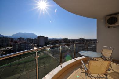 Licht Alanya balkon met glazen balustrade, zitplaatsen buiten en een panoramisch uitzicht op de stad en de bergen.