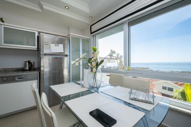 Bright Alanya kitchen featuring stainless steel appliances, a glass table, and panoramic sea views, creating a modern and airy atmosphere.