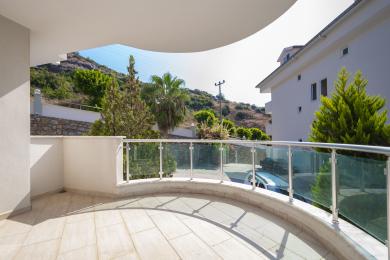 Alanya eiendom balkong med flislagt gulv, glassrekkverk og utsikt over frodig grønt og åssiden.