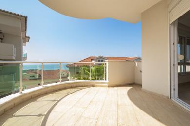 Balcon luminos în Alanya, cu balustrade de sticlă, podele din gresie și vederi uimitoare la mare sub un cer albastru senin.