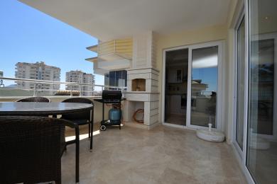 Alanya ejendom balkon med marmorgulve, udendørs spisesæt, indbygget grill og lys, solrig atmosfære.
