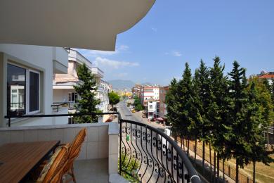 Alanya ejendom balkon med smedejerns gelænder, flisegulv og udsigt over byen på en solskinsdag.