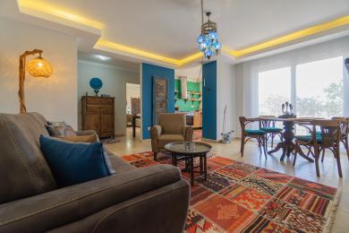 Alanya eiendom stue med fargerikt teppe, blå detaljer, varm belysning og åpen kjøkkenløsning som skaper en koselig atmosfære.