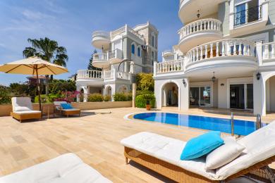 Alanya'da güneşli bir gökyüzü altında güneşlenme şezlongları, mavi havuz ve Akdeniz tarzı mimariye sahip villa havuz başı terası.
