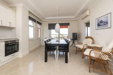 Яркая абедзенная зона ў Аланіі з кафлянай падлогай, сучасным чорным сталом, плеценымі крэсламі і выхадам на балкон.