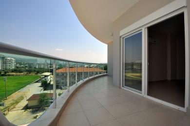 Balkon w Alanyi z szklanymi balustradami, wyłożony płytkami, z jasnymi i słonecznymi widokami na otaczający krajobraz.