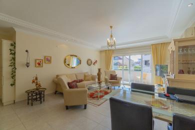 Alanya ejendom stue med adgang til balkon, neutrale toner, flisegulv og elegant lysekronebelysning.