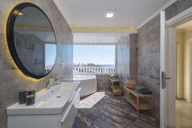 Alanya Badezimmer mit einem Whirlpool, modernem Waschbecken, Fliesen in Holzoptik und einem hellen Meerblick.