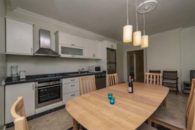 Alanya property kitchen featuring white cabinets, granite countertops, and warm pendant lighting above a wooden dining table.