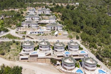 Alānijas īpašuma skats, kurā redzamas modernas villas ar privātiem baseiniem un balkoniem, kas atrodas kalna nogāzē.