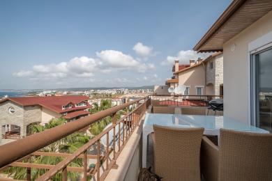 Alanya ejendom altan med kurvemøbler, glasbord og panoramaudsigt over byen og havet under en lys himmel.