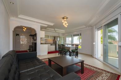 Světlý obývací pokoj v apartmánu v Alanyi nabízí moderní kuchyni, jídelní kout, přístup na balkon a pohodlnou koženou sedačku.