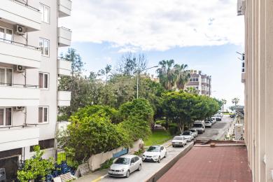Proprietate în Alanya cu vedere de la balcon spre copaci verzi luxuriante și mașini parcate într-o zi însorită.