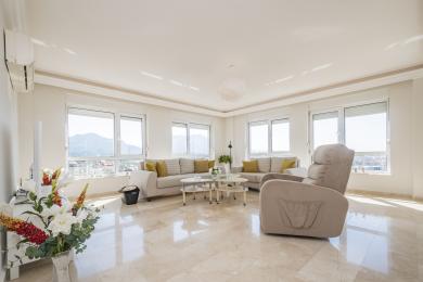 Lys Alanya stue med marmorgulv, nøytrale sofaer, store vinduer og fjellutsikt som skaper en rolig atmosfære.