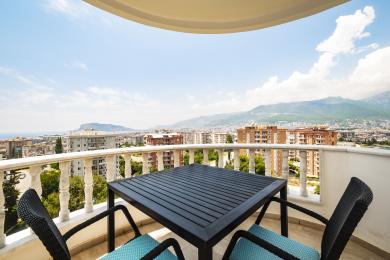 Alanya-Immobilienbalkon mit Tisch, Stühlen und Panoramablick auf die Stadt und die Berge im hellen Sonnenlicht.