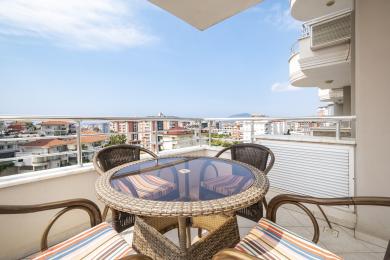 Alanya eiendom balkong med kurvmøbler, glassbord og panoramautsikt over byen under en lys, solrik himmel.