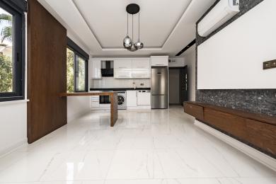 Beyaz dolapları, paslanmaz çelik aletleri, mermer zeminleri ve benzersiz ahşap kahvaltı barı ile aydınlık, modern Alanya mutfağı.