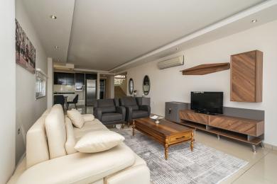 Helles Wohnzimmer in Alanya mit cremefarbenem Sofa, grauen Sesseln, Holzmöbeln und einer offenen Küche.