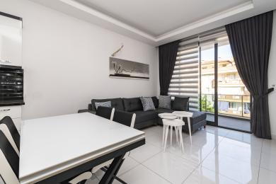 Lys Alanya lejlighed stue med adgang til balkon, med en grå sofa, hvidt bord og flisegulv.