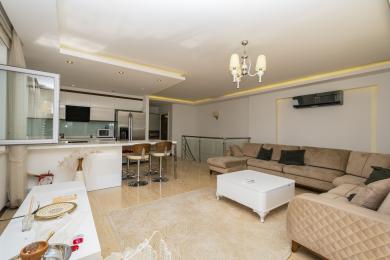 Alanya eign: Björt, opið alrými með nútímalegu eldhúsi, beige sófa og fáguðu flísalögðu gólfi.