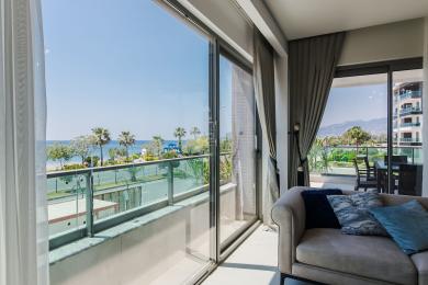 Alanya Wohnzimmer mit einem Sofa und einem Balkon mit Blick auf das türkisfarbene Meer und Palmen.