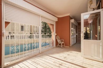 Proprietate în Alanya cu balcon cu podea de gresie, pereți de teracotă, elemente metalice albe și vedere la piscină în lumina puternică a soarelui.