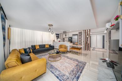 Lyst, åbent Alanya-opholdsrum med moderne køkken, bløde sofaer, marmorgulve og elegant, varm belysning.