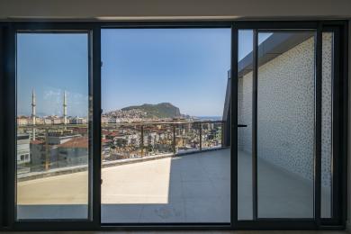 Bright Alanya balcony with glass railings offers stunning city and sea views through large sliding glass doors.