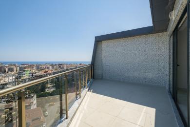 Alanya ejendom balkon med glasrækværk, flisegulv, mosaikvæg og panoramaudsigt over byen og havet.