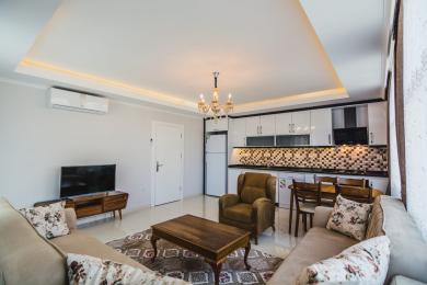 Alanya Apartment Wohnzimmer mit offener Küche, modernen weißen Schränken, warmer Beleuchtung und bequemen Sitzgelegenheiten.