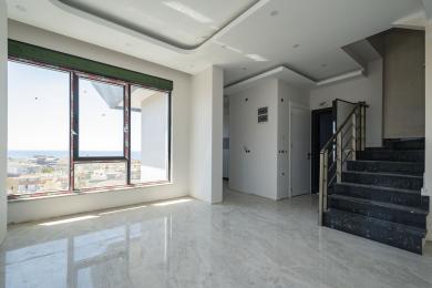 Šviesus Alanya būsto interjeras su marmurinėmis grindimis, laiptais ir dideliais langais, iš kurių atsiveria vaizdai į jūrą.