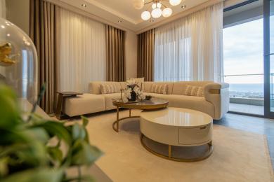 Alanya property living room featuring a beige sectional sofa, gold accents, soft lighting, and balcony access with sea views.