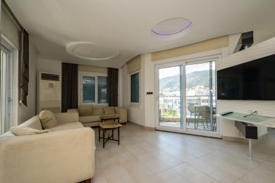Alanya eiendom stue med beige sofa, flislagte gulv, balkongtilgang og moderne belysning.