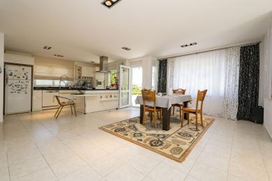 De lichte Alanya woning keuken en eetgedeelte beschikt over witte kasten, tegelvloeren en een houten eethoek op een patroonkleed.