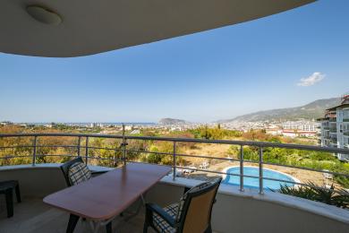 Alanya kinnisvara rõdu laua, toolide ning panoraamvaatega linnale, merele ja basseinile.