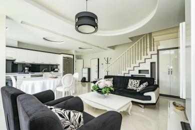 Lys, åpen stue i Alanya med moderne hvitt kjøkken, trapp og stilige svart-hvitt møbler.
