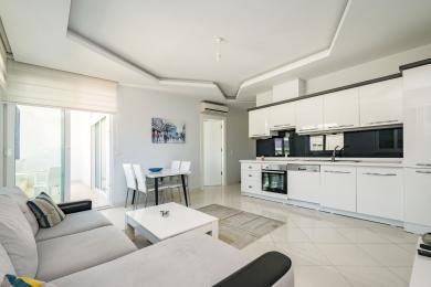 Lys Alanya lejlighed stue med hvidt køkken, spiseplads, adgang til balkon og moderne, luftig atmosfære.