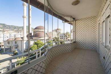 Alanya eiendom balkong med glassinnhegning, flislagt gulv og vegger, som tilbyr lys utsikt over byen og moskeen.