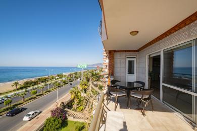 Alanya mülkündə mərmər döşəmə, yemək dəsti və parlaq, günəşli atmosferə malik dəniz mənzərəli balkon.