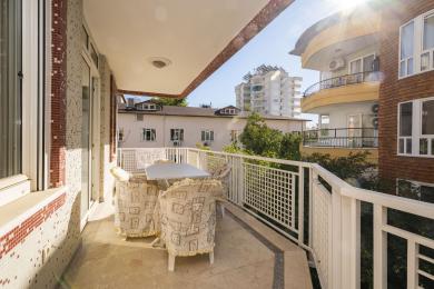 अलान्या में एक उज्ज्वल बालकनी जिसमें मोज़ेक दीवारें, टाइल फ़्लोरिंग और आउटडोर डाइनिंग सेट है, जो एक आरामदायक माहौल बना रहा है।