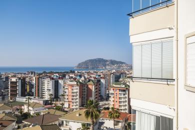 Alanya ejendom altanudsigt, der viser by-, hav- og bjergudsigter gennem glaspaneler, badet i klart sollys.