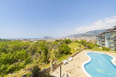 धूप वाले दिन अलाया में शहर, समुद्र और पहाड़ों के नज़ारे वाले पत्थर के आँगन के साथ एक पूल।