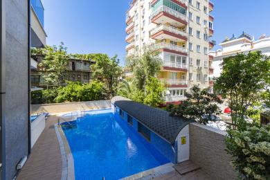 Alanya eiendom som viser et lyseblått svømmebasseng med en overbygd seksjon og uteområde.