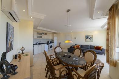 Proprietate în Alanya, cu o zonă de living open-space, cu o bucătărie, masă de sufragerie și o canapea confortabilă, toate iluminate de o lumină naturală caldă.