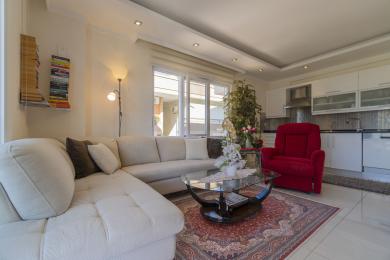 Helles Wohnzimmer in Alanya mit einem weißen Sofa, einem roten Sessel und einer modernen offenen Küche.