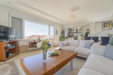 Helles, offenes Alanya-Wohnzimmer mit weißen Sofas, Holzakzenten und Blick auf die Stadt.