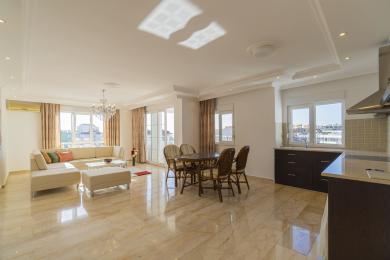 अलान्या में संगमरमर के फर्श, एक आधुनिक रसोई और झूमर के नीचे आरामदायक बैठने की व्यवस्था वाला एक उज्ज्वल, ओपन-प्लान लिविंग एरिया।