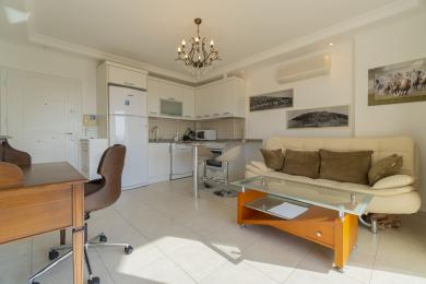 Svijetli apartman u Alanji, dnevni boravak s bijelom kuhinjom, radnim stolom, sofom i podovima od pločica.